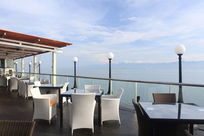 Chairs and tables at restaurant by sea against sky