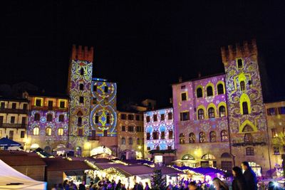 People on illuminated buildings in city at night
