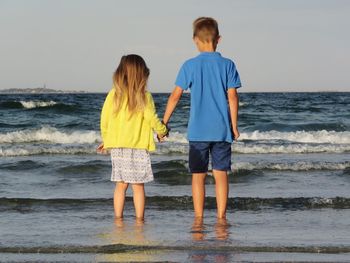 Rear view of siblings holding hands while standing on shore