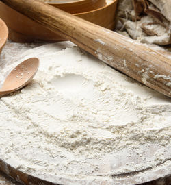 White wheat flour and wooden rolling pin on board, baking ingredients, close up
