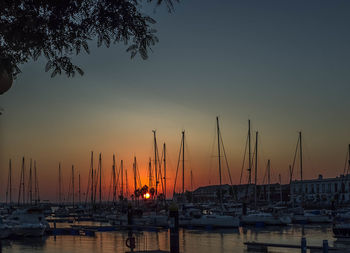 Sailboats moored on harbor against clear sky during sunset