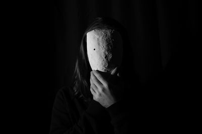 Portrait of woman covering face against black background