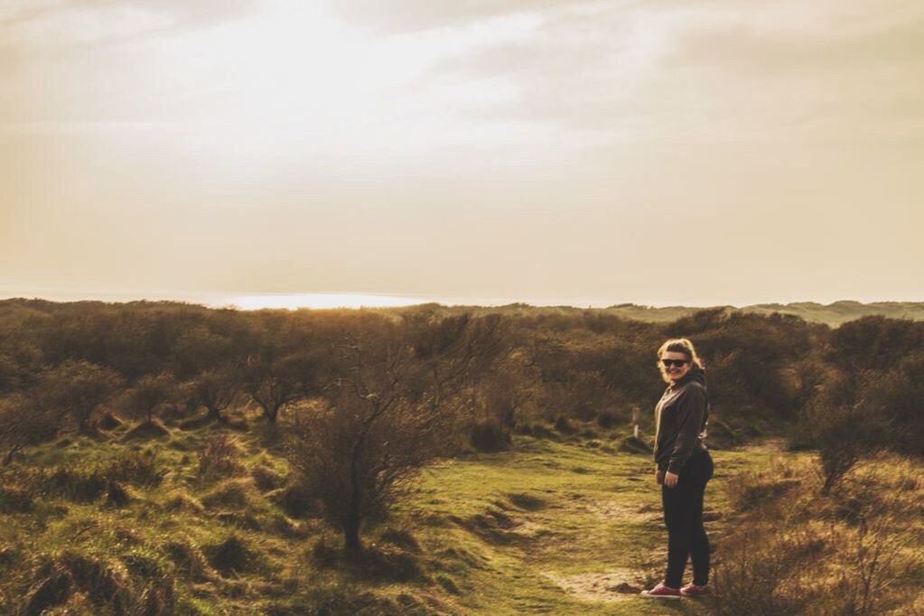 lifestyles, leisure activity, casual clothing, standing, field, full length, landscape, sky, tranquility, young adult, tranquil scene, rear view, nature, three quarter length, grass, beauty in nature, scenics, person