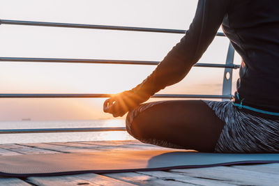 Low section of woman relaxing on railing by sea against sky