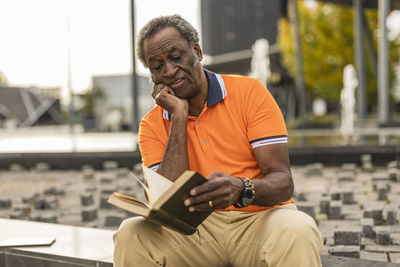 Senior man with hand on chin reading book