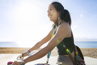 Side view of happy sporty woman riding bicycle by beach