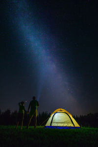 People standing by tent on field against sky at night