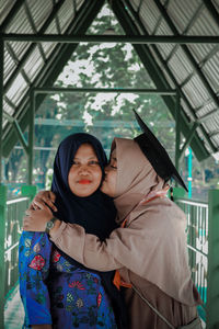 Young woman with mortarboard kissing mother standing on footpath