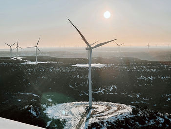 Wind turbines on land against sky during sunset