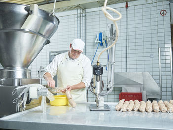 Butcher making fresh sausages through machinery in factory