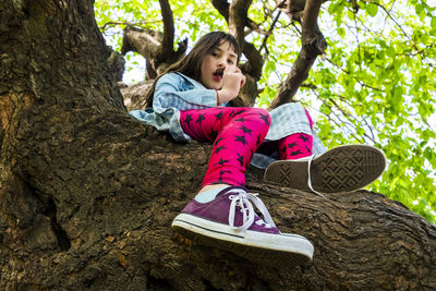 Full length of girl sitting on tree trunk