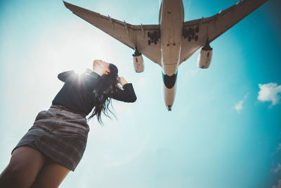 Woman looking at airplane flying against sky