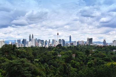 Trees and buildings in city against sky