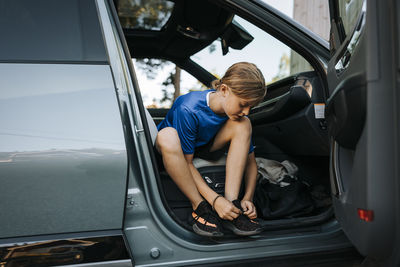 Full length of boy tying shoelace while sitting in car