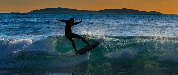 Silhouette man jumping in sea against sky during sunset