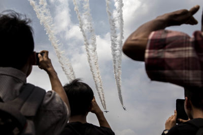 Rear view of people photographing airshow against sky