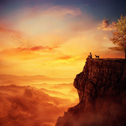 Man with faithful dog stand on the peak of a cliff watching sunset over valley. recalling childhood