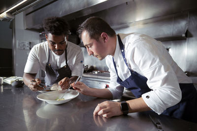 Concentrated multiethnic professional cooks preparing meal with slice of fish on ceramic plate in restaurant while working together