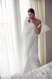 Young woman in a white towel after a spa is standing in the room at the door with tea in her hands