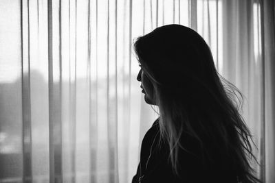 Thoughtful woman looking through window at home