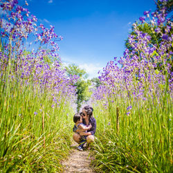 Mother crouching with daughter amidst lavender flowers on field against sky