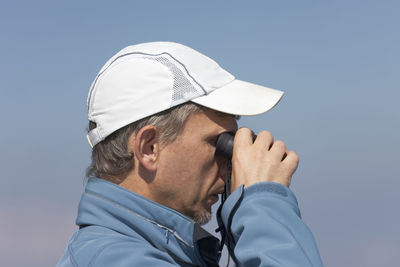 Side view of man looking through binoculars against clear sky