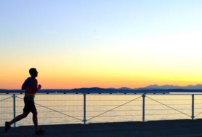 Side view of man running by lake against sky