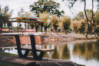 Empty bench in park by lake against sky