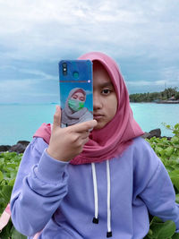 Portrait of young woman using smart phone against sky
