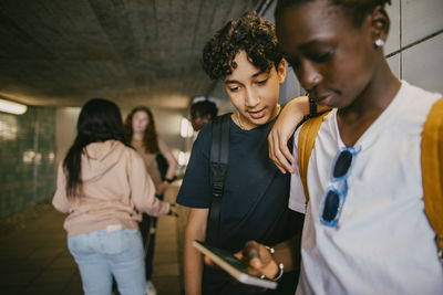 Teenage boy standing with male friend using smart phone in underground tunnel