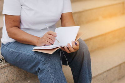 Midsection of woman reading book while sitting on sofa at home