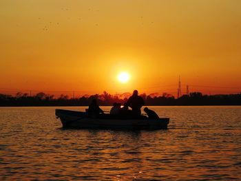 Silhouette people in boat on sea against orange sky