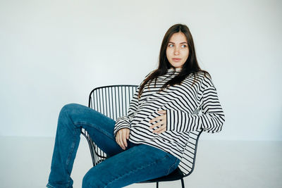 Pregnant attractive woman sits on a chair in the studio.