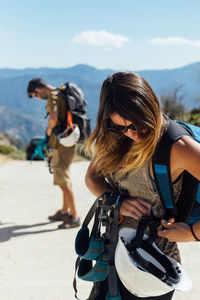 Side view of female adventurer in activewear with helmet and equipment for rappelling fastening belts while preparing for training with friend in mountains