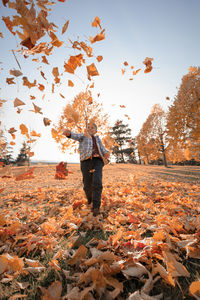 Rear view of person standing by leaves during autumn