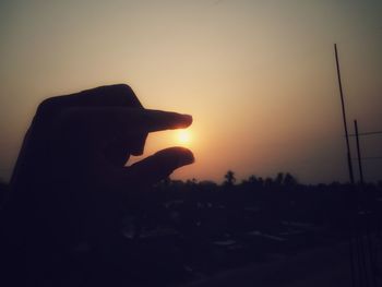 Close-up of silhouette hand holding sun during sunset