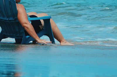 Low section of woman sitting on chair at beach