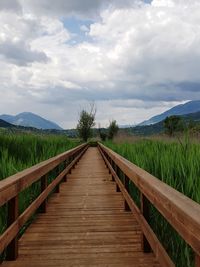 View of wooden boardwalk leading towards mountains against sky