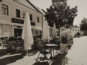 Empty chairs and tables at sidewalk cafe amidst buildings