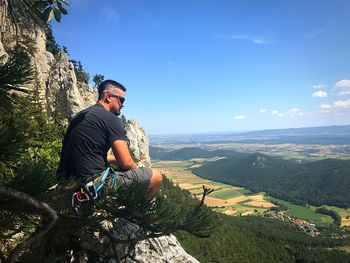 Young man sitting on rock against mountains