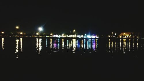Illuminated city by river against sky at night