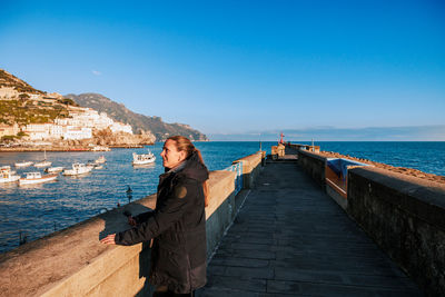 Rear view of woman standing at beach against clear blue sky