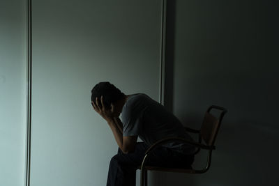 Side view of sad man with head in hands sitting on chair