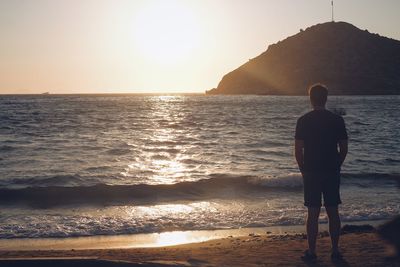 Rear view of man looking at sea during sunset