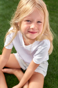 Portrait pretty smiling blonde girl sitting on green grasson field mock up white t shirt top view.