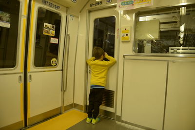 Full length rear view of boy peeking through door while boarding metro train