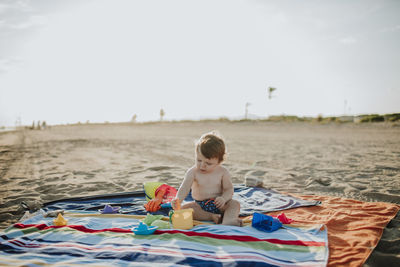 Male toddler playing with toys at beach during sunset