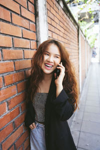 Portrait of smiling young woman standing against brick wall