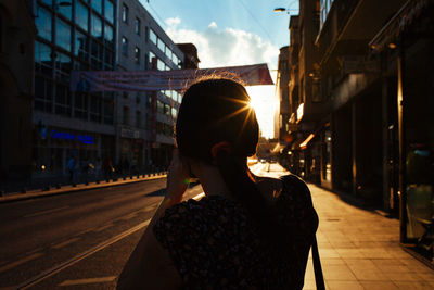 Rear view of mid adult woman photographing while standing on sidewalk in city