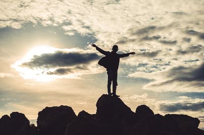 Silhouette man standing on rock against sky